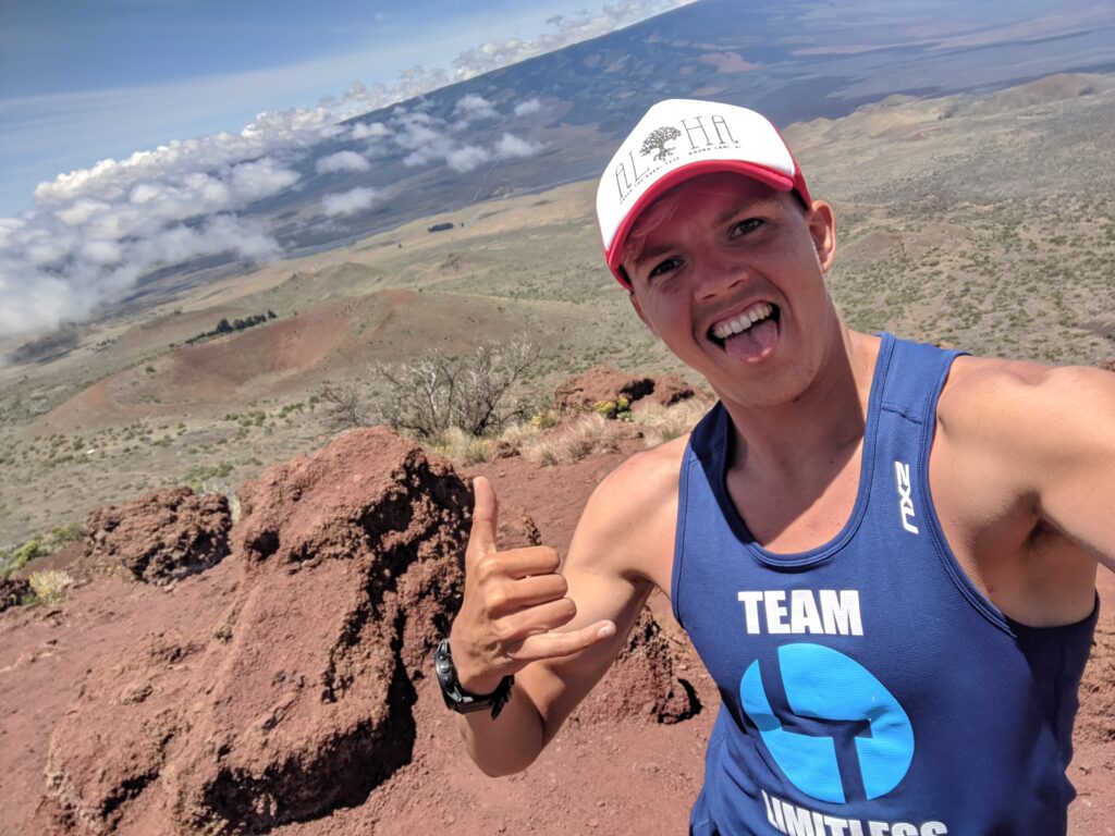Journey Endurance coach smiling and giving a shaka sign on the rugged volcanic landscape of Mauna Kea, Hawaii, during high-altitude training.