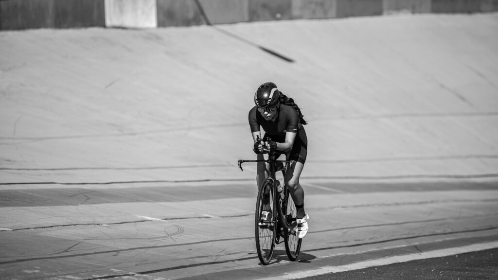Dynamic black and white photo of a cyclist racing in an urban setting, capturing speed and determination.