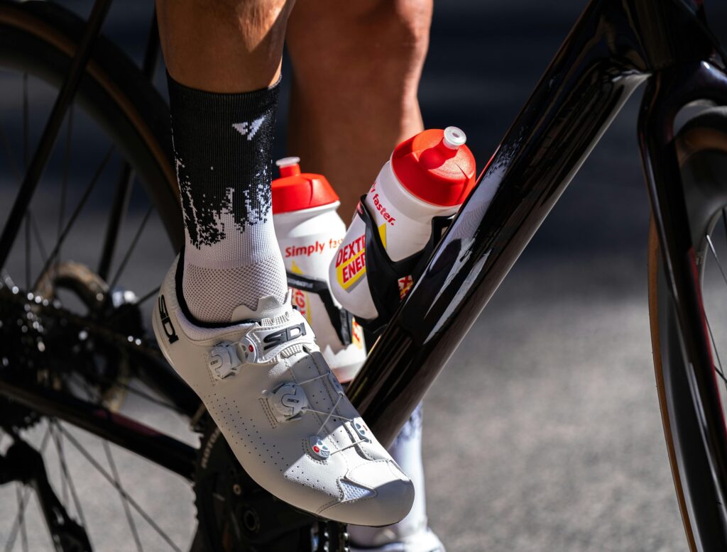 Cyclist's shoe on pedal with energy drink bottles attached to bike frame.